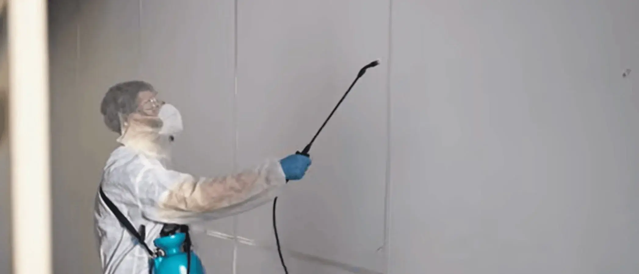 Indoor pest treatment along a wall in protective gear